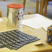Auf einem Tisch liegen die Klebestreifen mit dem Segenskürzel und zwei Spendendosen