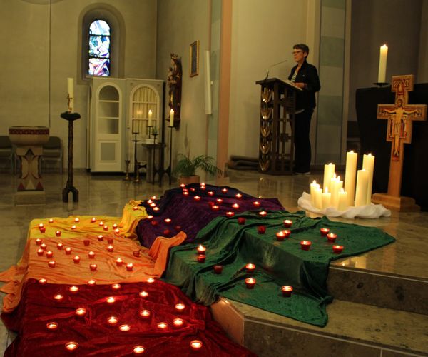 Frau am Ambo, im Vordergrund Kerzen vor dem Altar und das Franziskuskreuz